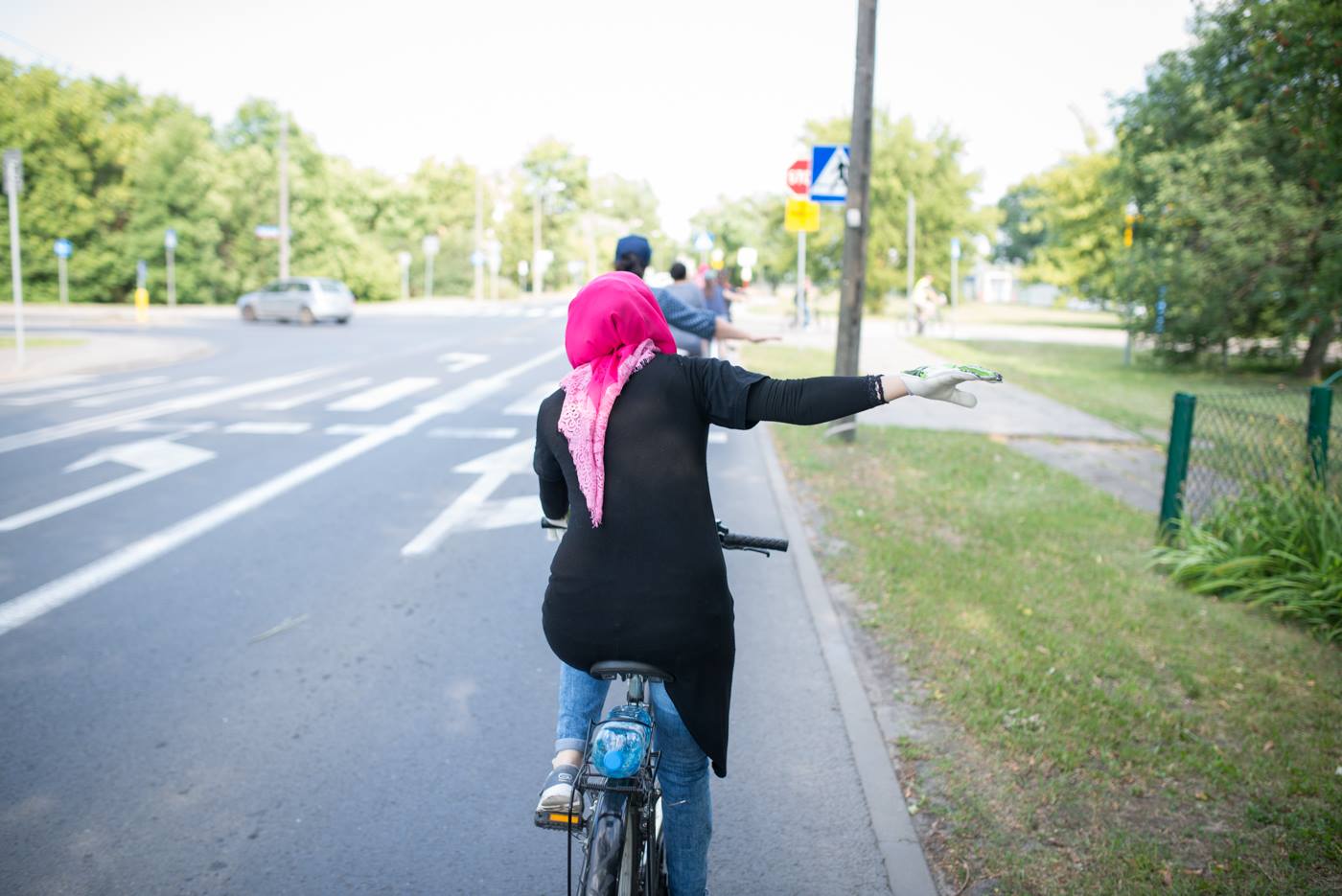 Na zdjęciu uchodźczyni na rowerze w chuście, wyciągająca prawą rękę sygnalizując zamiar skrętu w prawo